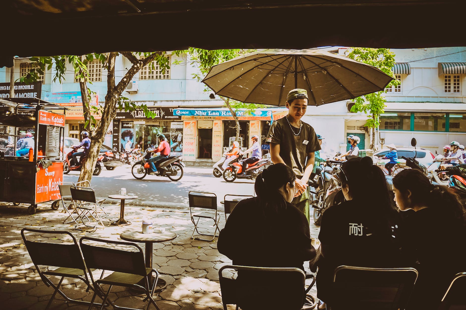 man standing beside umbrella facing three women sitting on chairs