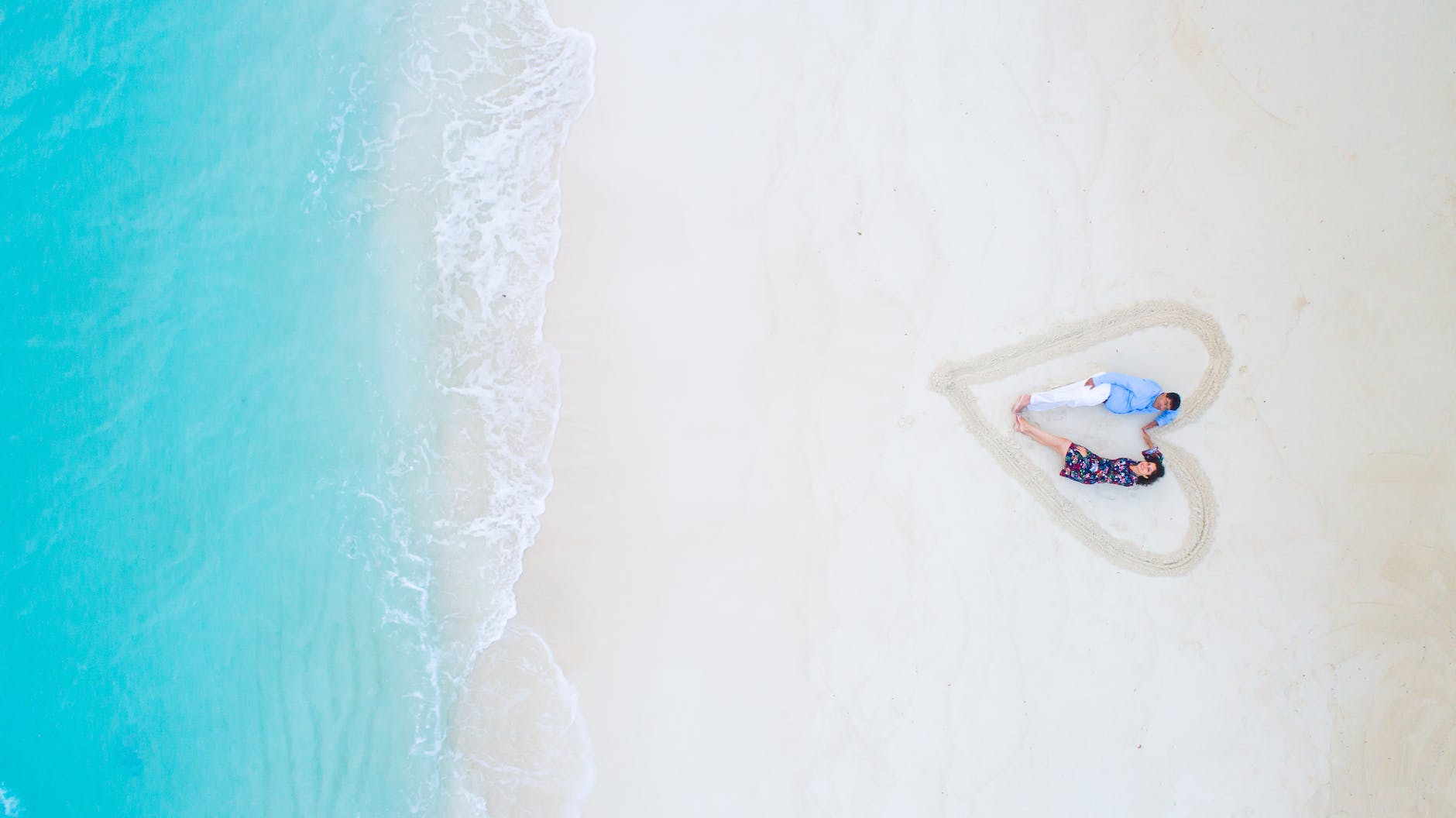 man and woman lying on white sand near sea shore